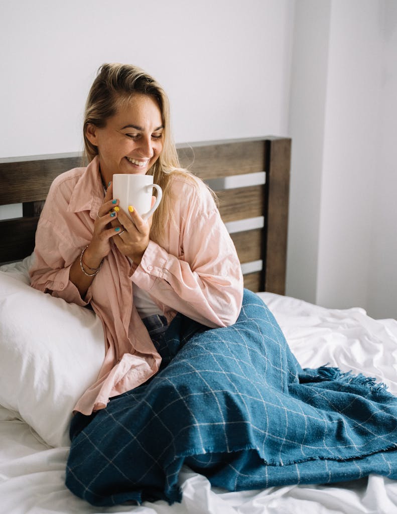 A woman enjoying a warm beverage under a blanket on a cozy morning in bed.